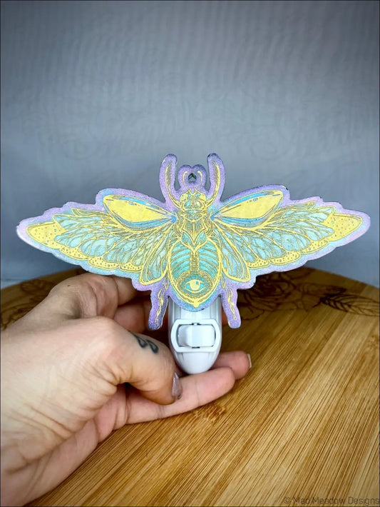 A stunning iridescent scarab resin wall night light with mesmerizing pastel purple and aqua blue hues on a plug-in base