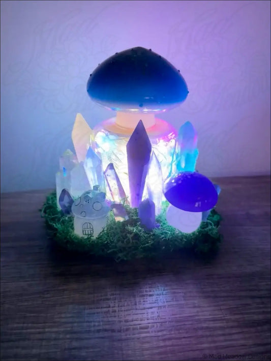 A glowing blue usb light shaped like a mushroom with crystal accents and a miniature house in green moss