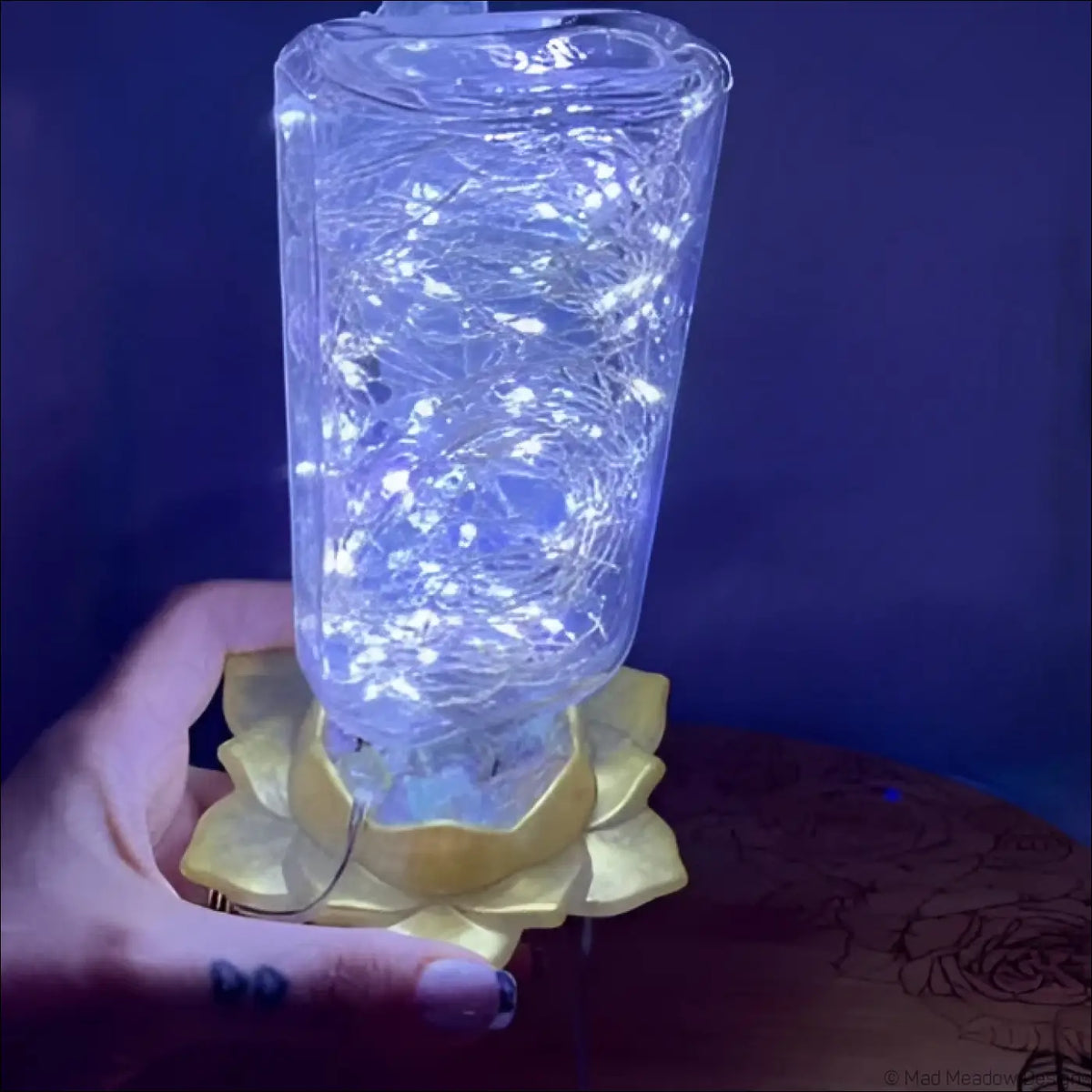 A clear antique glass apothecary bottle lantern with white fairy lights resting on a golden lotus flower base usb light