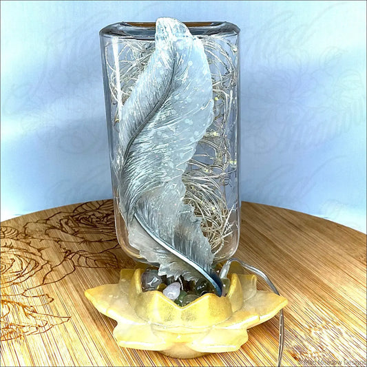 Silver feather sculpture inside a clear glass apothecary bottle resting on a yellow lotus base usb light