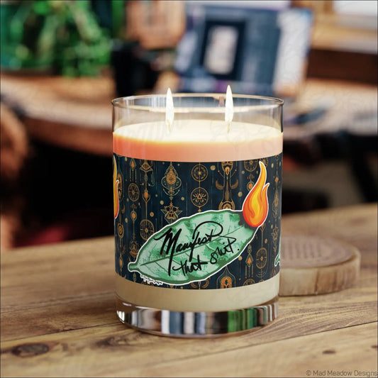 A clear glass candle with two lit wicks and a teal label featuring gold mystical symbols for spiritual rituals