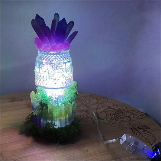 A glowing glass jar lamp with purple and pink crystals and green moss accents lit by soft white usb light