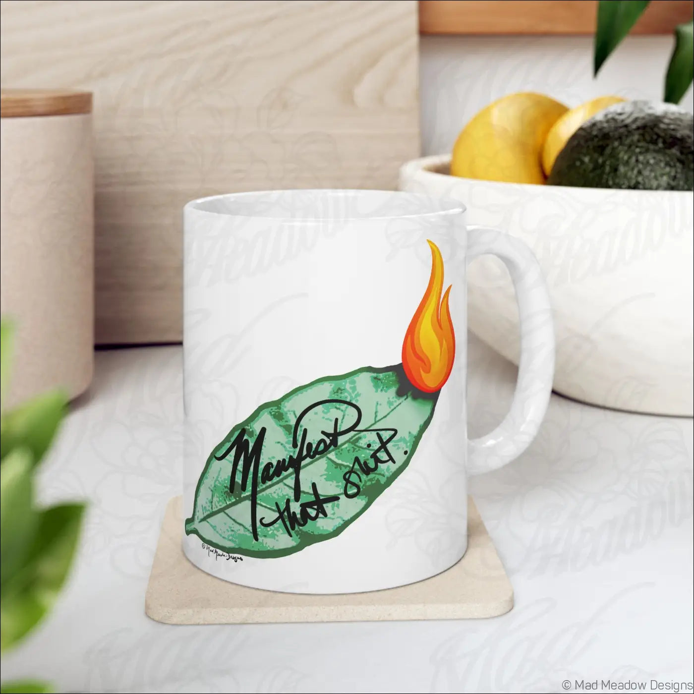 Glossy white ceramic mug with comfortable c handle featuring hand drawn flaming leaf and manifest that shit text