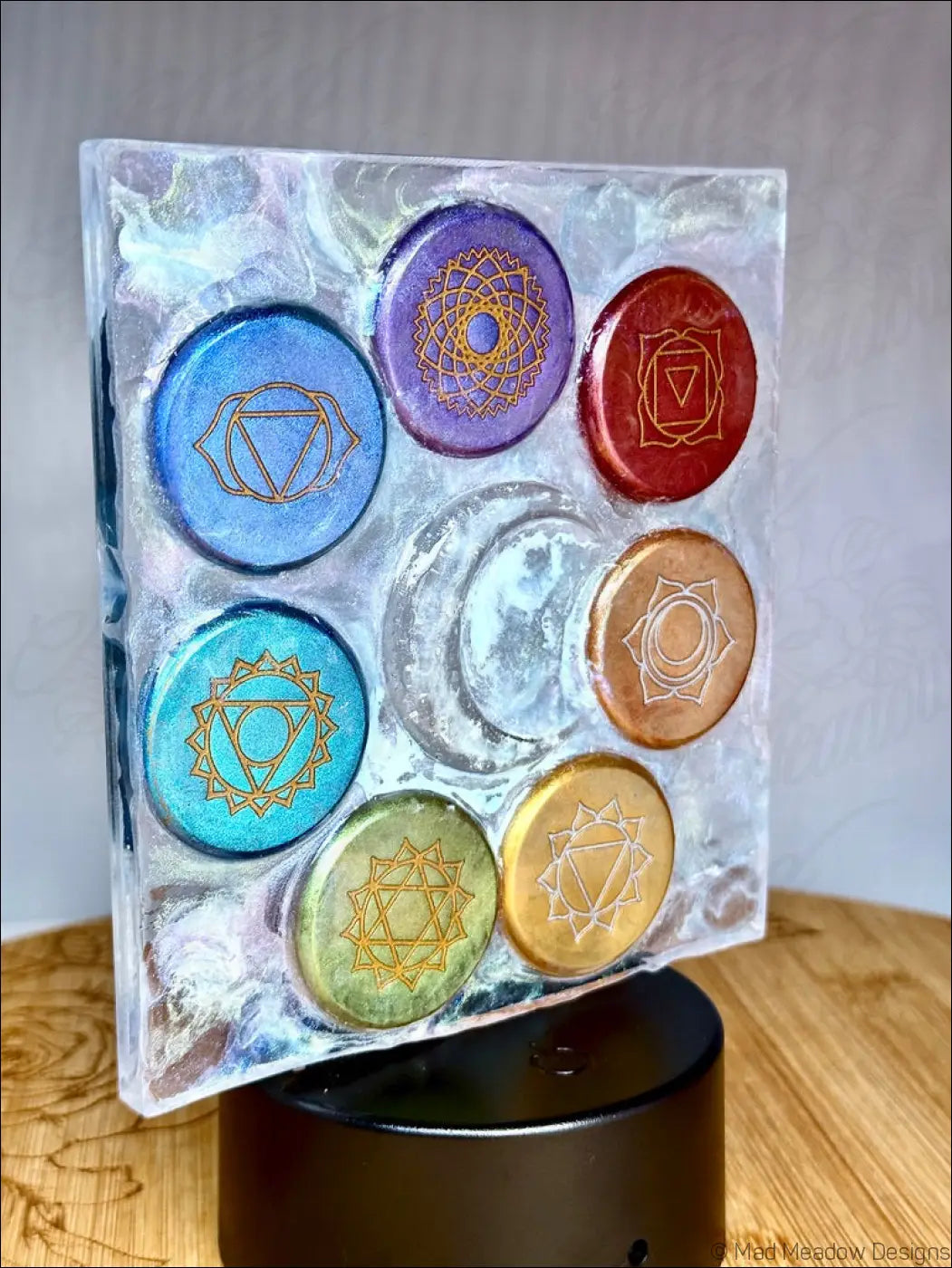 A clear resin chakra night light with rainbow-colored disks arranged around a glowing crescent moon symbol