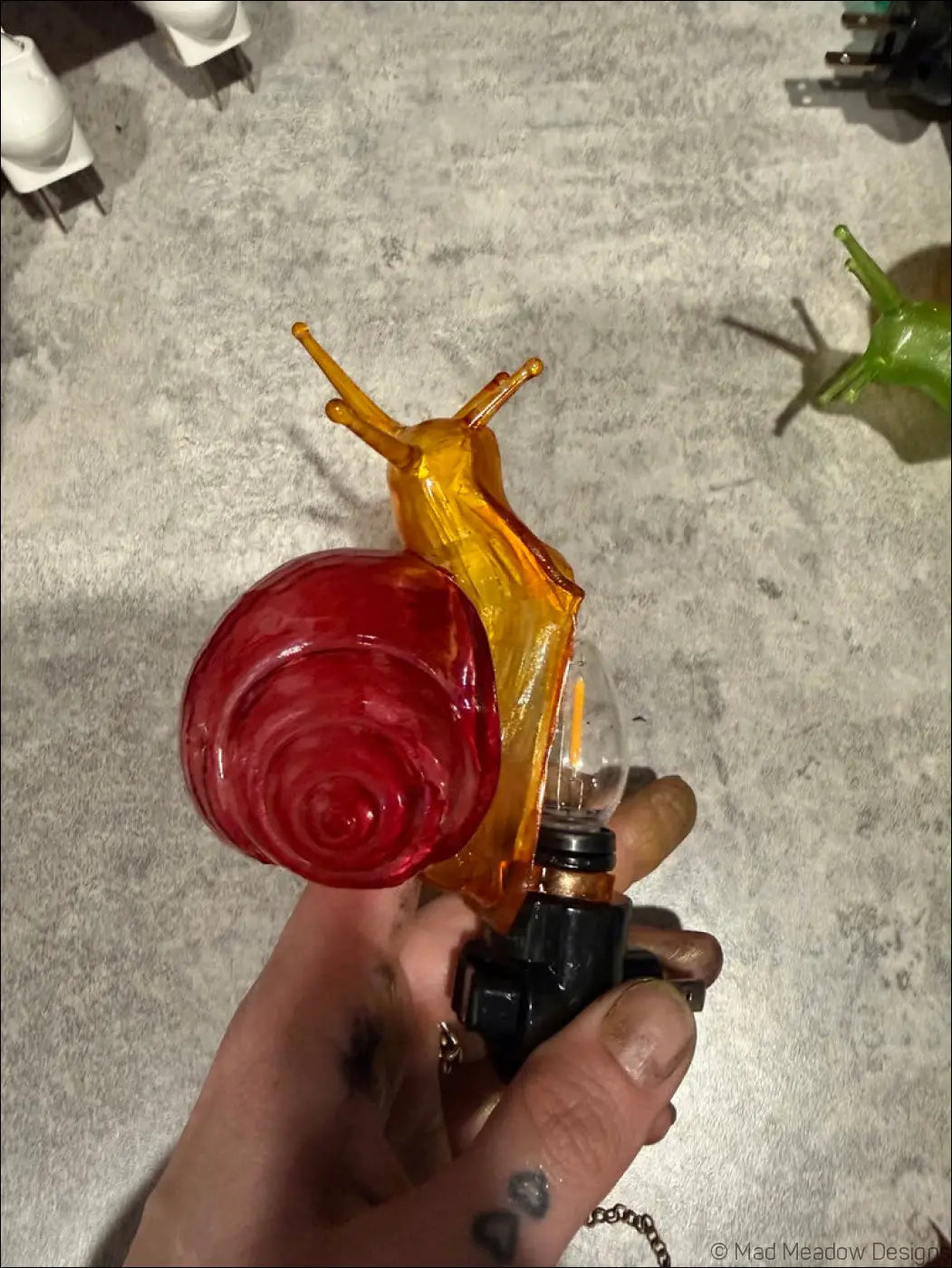 Charming snail night light with translucent orange glass body and vibrant red shell featuring exposed bulb and black base