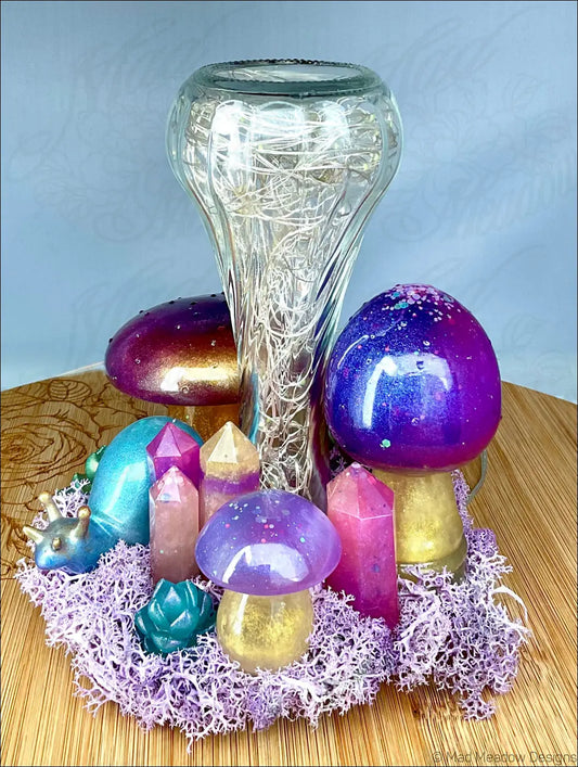 A clear glass vase with intricate wirework surrounded by colorful handcrafted resin mushrooms crystals and a snail companion on purple moss tabletop light