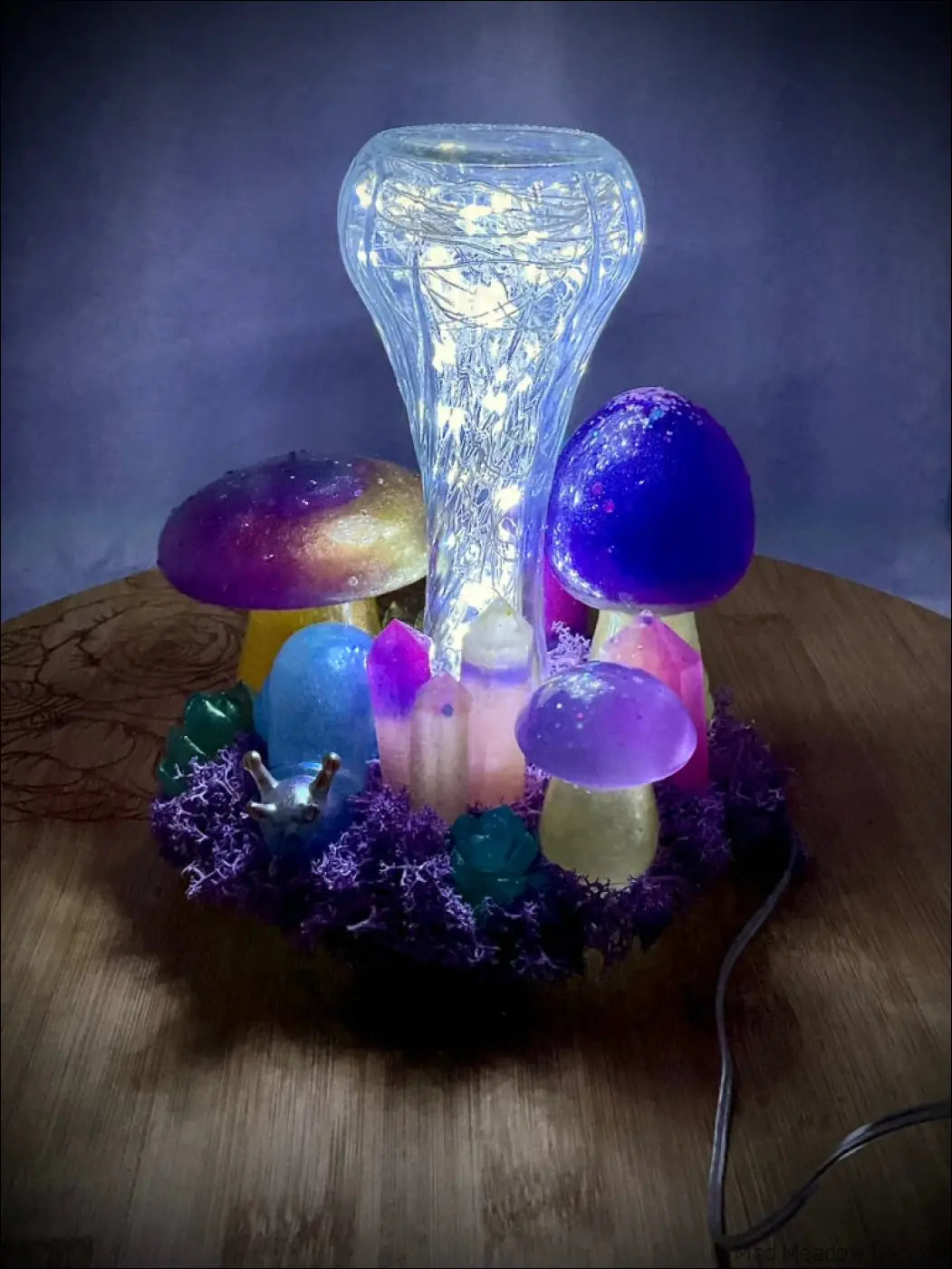 A glowing tabletop light with handcrafted resin mushrooms, a snail companion, and fairy lights on purple moss
