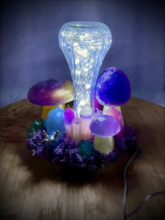 A glowing tabletop light with handcrafted resin mushrooms, a snail companion, and fairy lights on purple moss