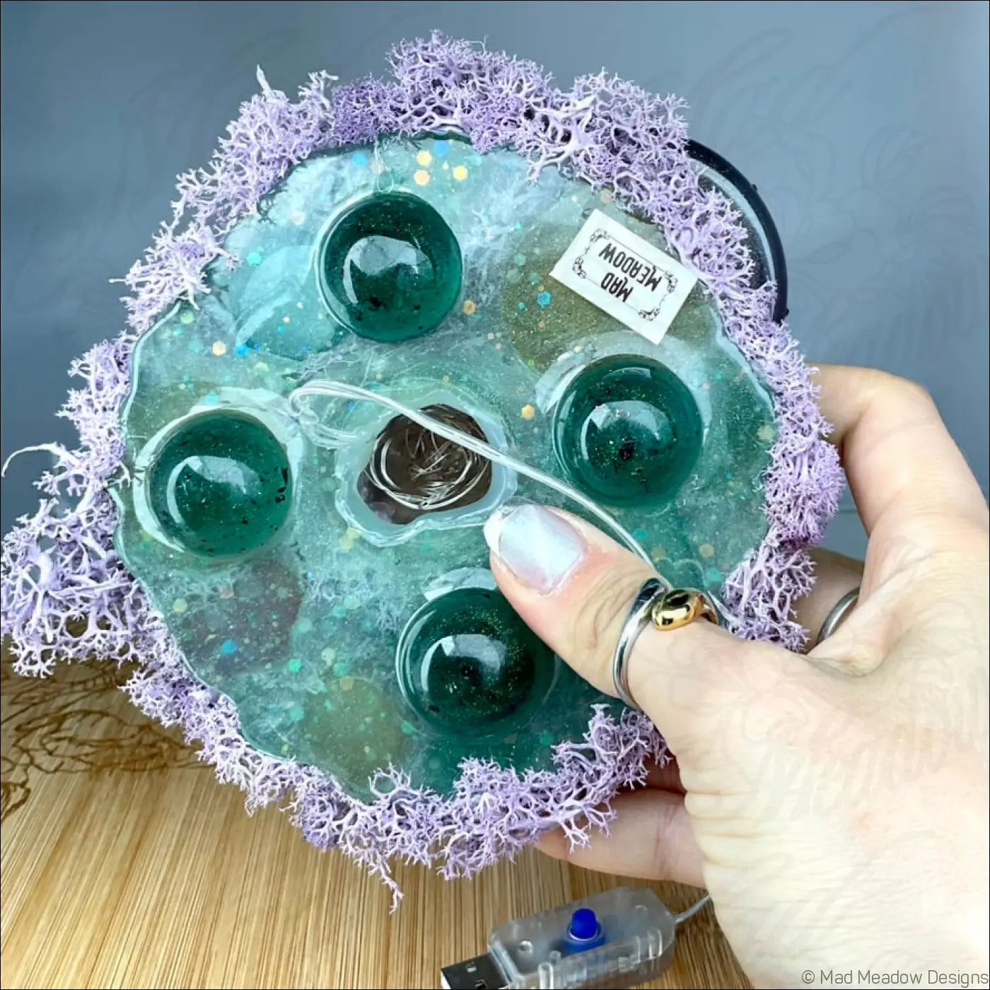 A teal handcrafted resin stress ball with green glass orbs and purple moss border from m80 meadow tabletop light