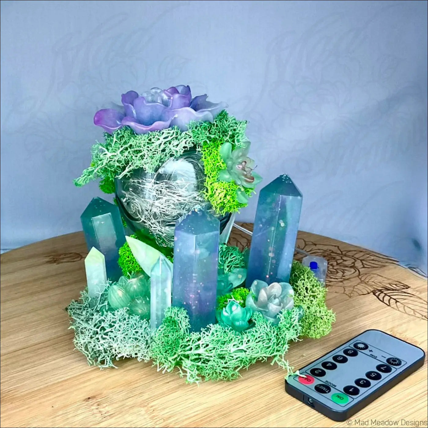 A usb powered vintage glass bottle centerpiece with teal resin, crystal pillars, moss, and purple flowers