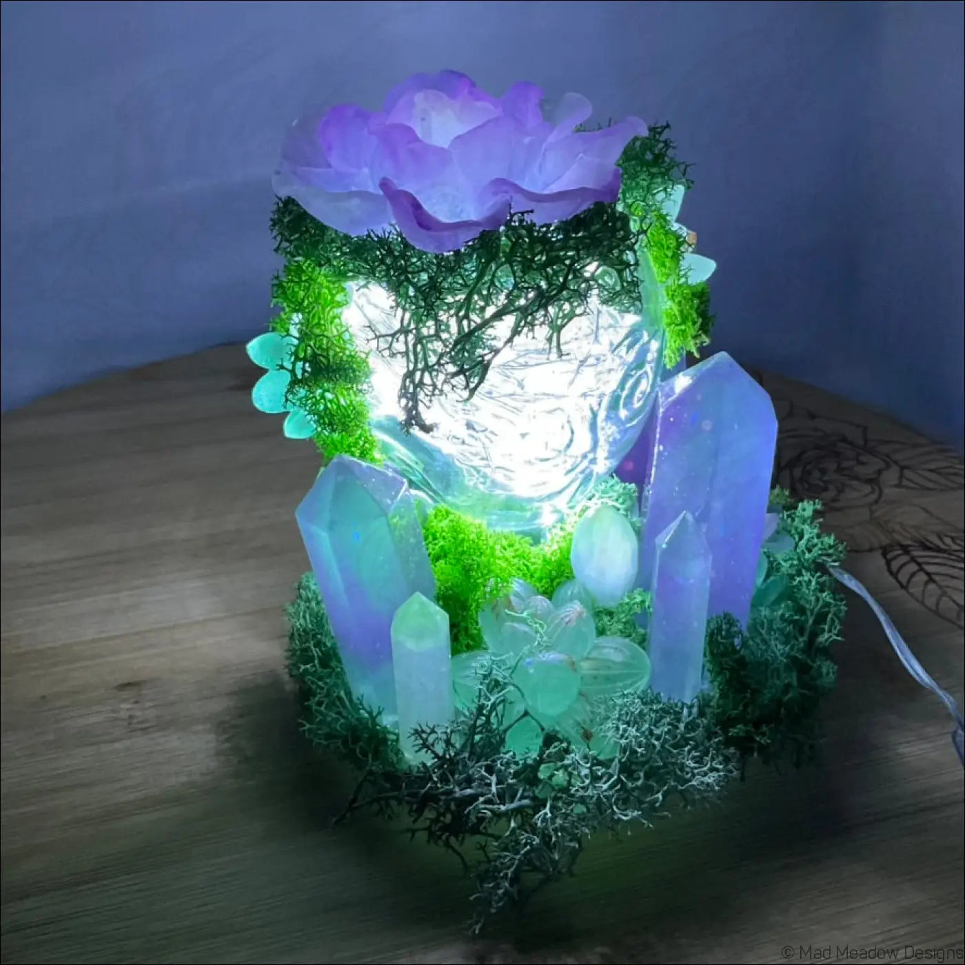 A glowing crystal filled garden light with vibrant moss and purple flower in a usb powered vintage glass bottle