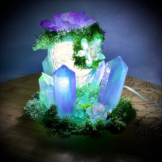 A glowing blue and purple crystal garden light with artificial moss on a vintage glass bottle usb powered centerpiece