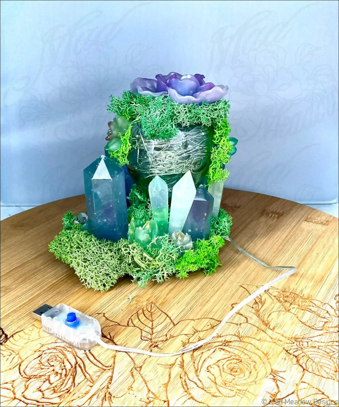 A usb powered vintage glass centerpiece with green moss, purple flower, and blue-green crystal pillars lighting up