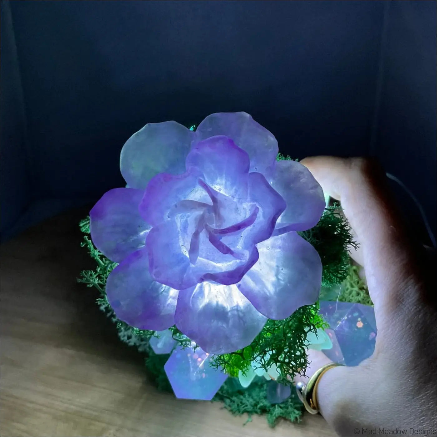 A glowing purple flower lamp with layered petals on green moss and crystals in a usb powered vintage glass bottle