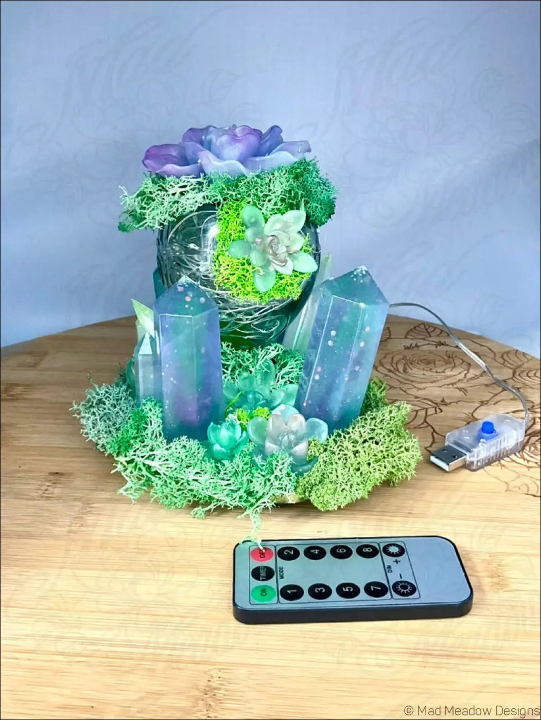 A usb powered vintage glass bottle light with a glowing resin centerpiece of purple and green succulents and moss