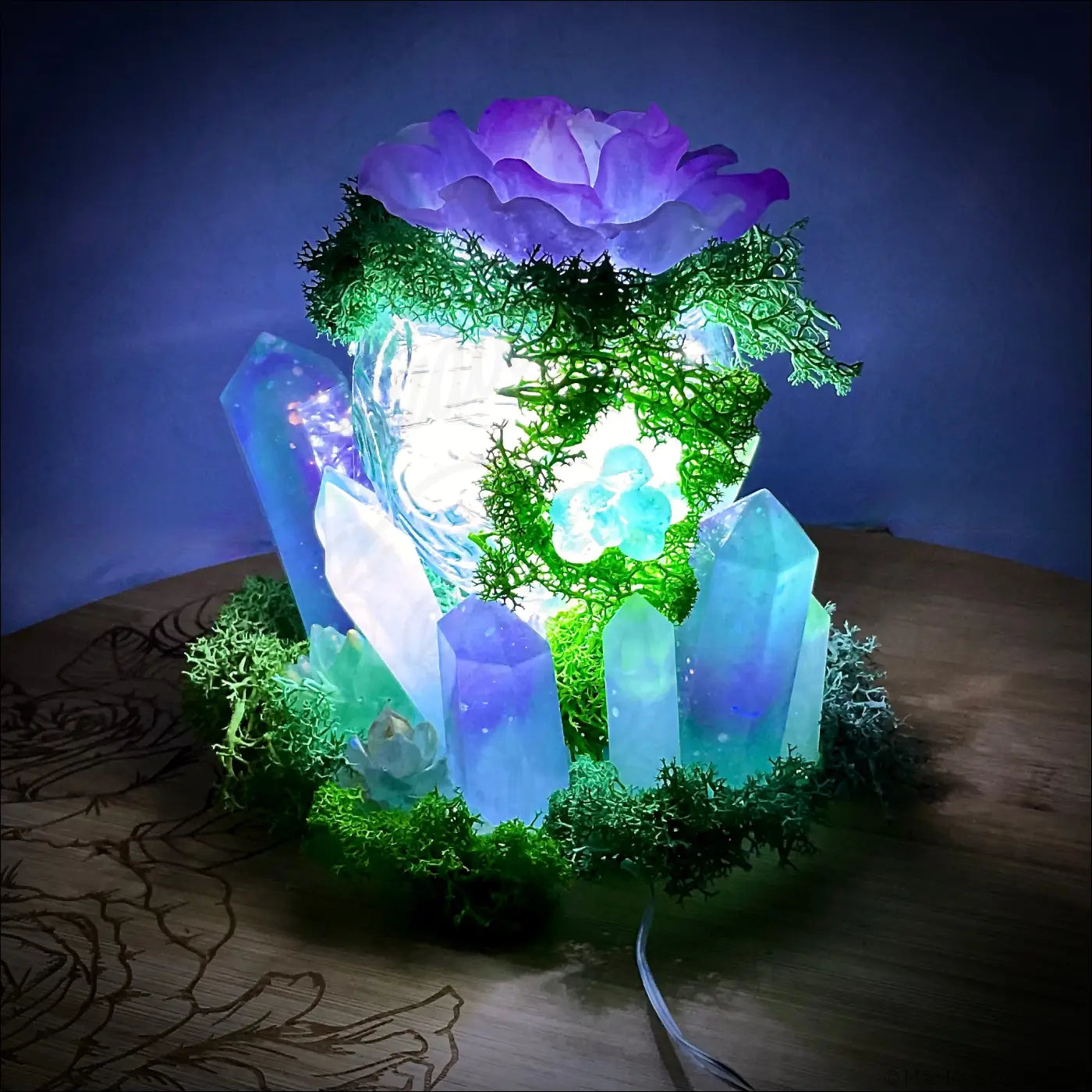 A usb powered vintage glass lamp with a purple flower, green moss, and blue white crystal decorations glowing warmly