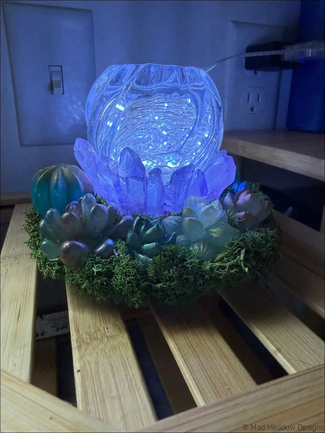 Blue glowing usb powered glass orb lamp with crystal facets and lotus base surrounded by moss and succulents