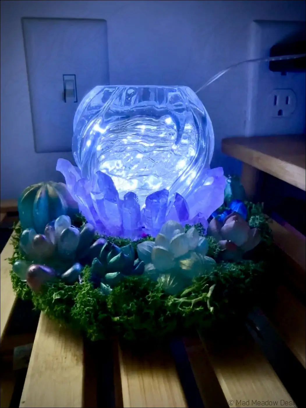 A usb powered glowing blue crystal bowl centerpiece with embedded lights surrounded by succulents and moss