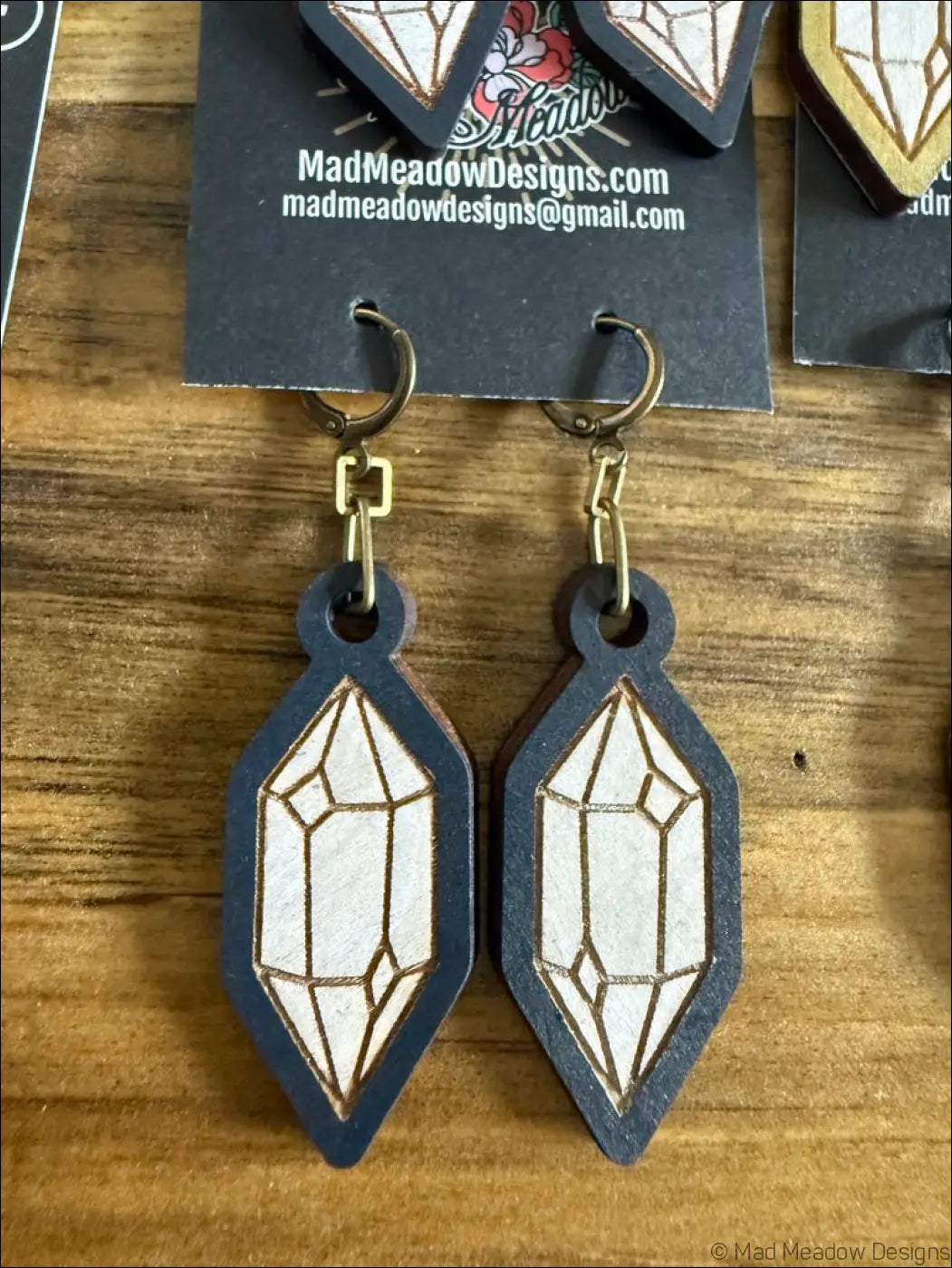 A pair of dark blue wooden earrings shaped like geometric crystals with white and gold laser-cut details and brass hooks