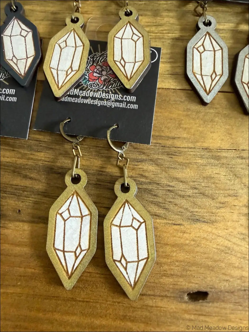 Gold-toned wooden earrings shaped like geometric crystals with white inlay and brown line detailing
