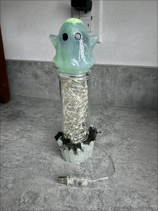 A cute translucent green ghost usb lamp with black eyes glows on a jar of white string lights and crystals