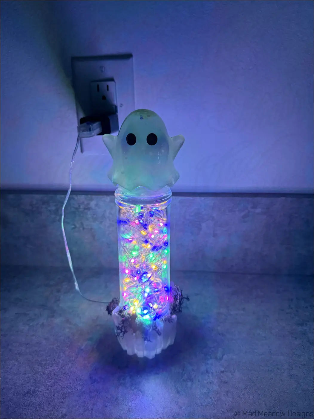 A cute glowing ghost usb light with a clear glass jar base filled with colorful flashing lights moss and crystals