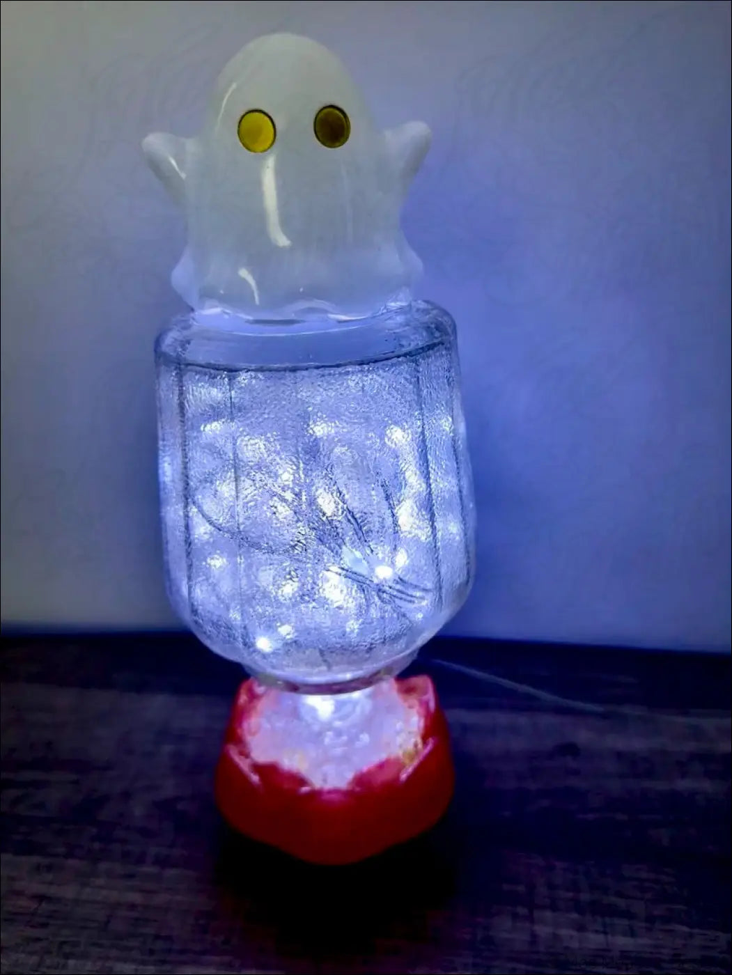 A cute glowing white ghost figurine with yellow eyes sits on a vintage glass bottle filled with usb fairy lights