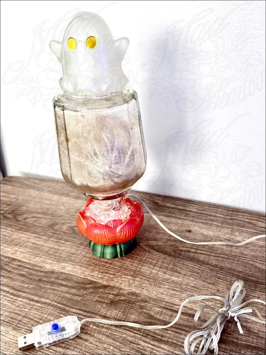 A cute glowing ghost usb light with yellow eyes on a vintage glass bottle and red green flower base with fairy lights