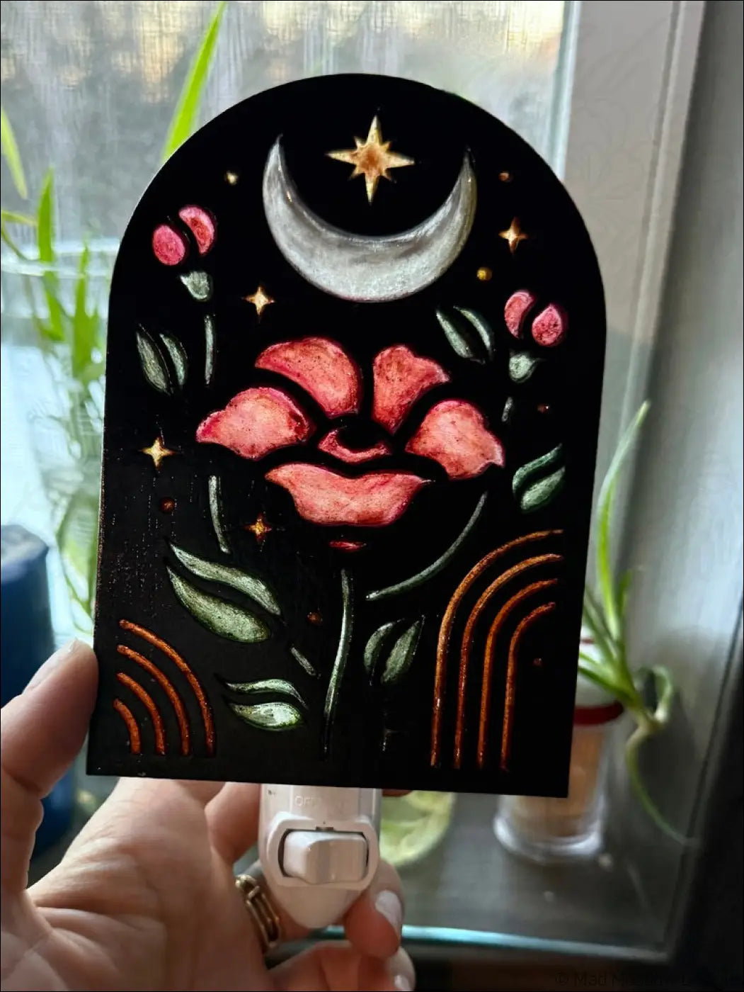 A black arched plug-in night light with elegant flowers pink petals green leaves and a silver moon star design