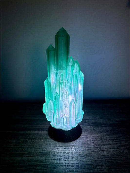 A glowing teal crystal lamp with a black base hand inked 3d printed for a mystical sanctuary printed emerald city night light