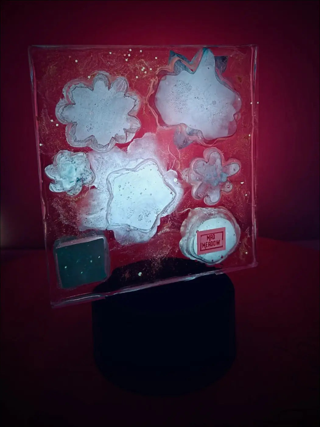 A translucent red glass pastel garden nightlight with white and teal floral shapes and a mad meadow label in dreamy hues