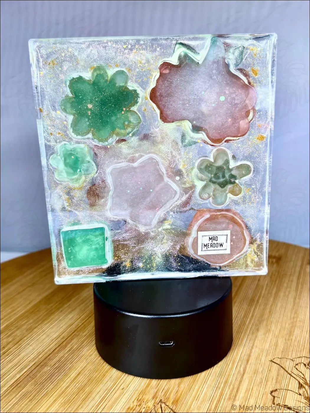 A square resin coaster with embedded green pink and clear succulent molds and gold flecks for a pastel garden nightlight