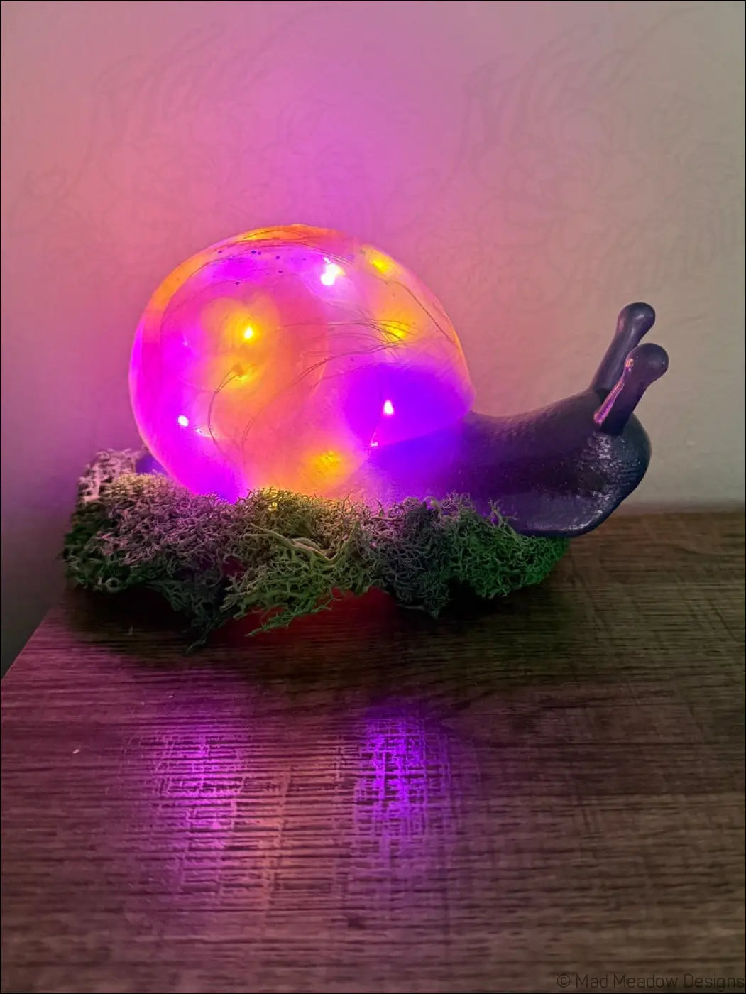 A glowing giant pastel blue and purple snail led lamp with a translucent shell resting on green moss light usb color change