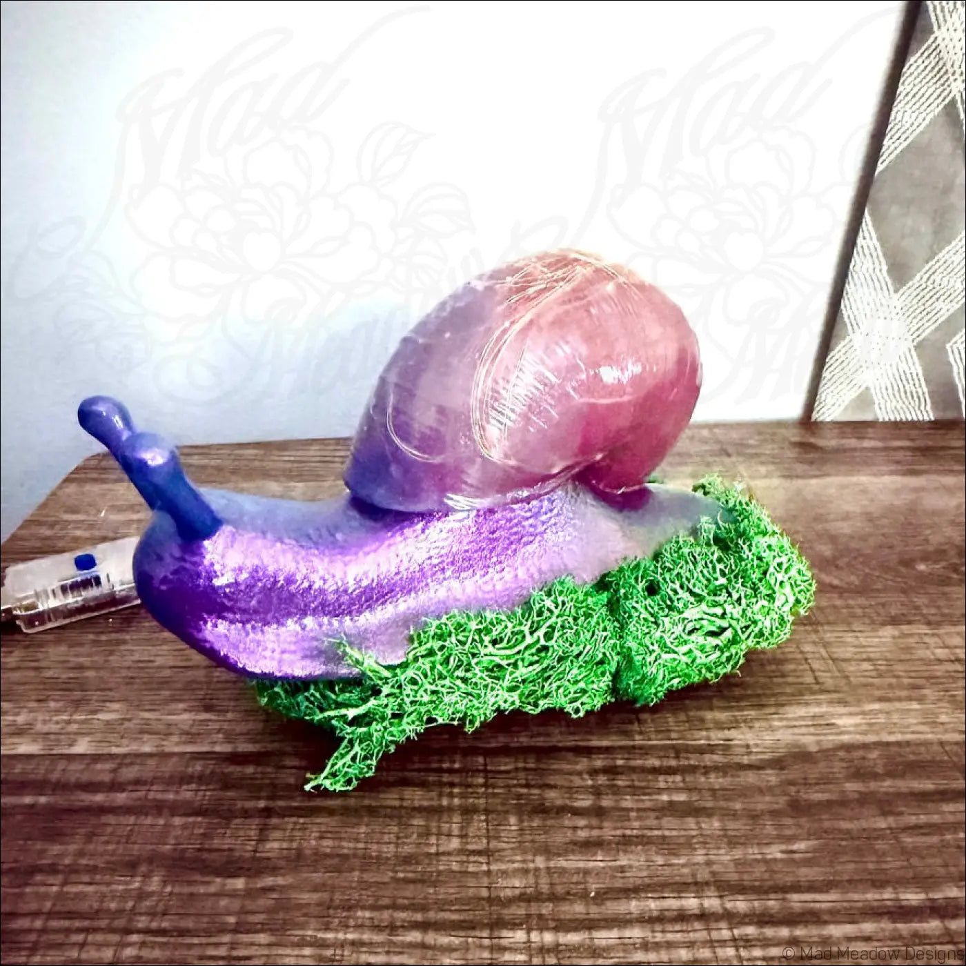 A glossy purple snail figurine with a translucent pink shell on vibrant green moss in a usb color change light
