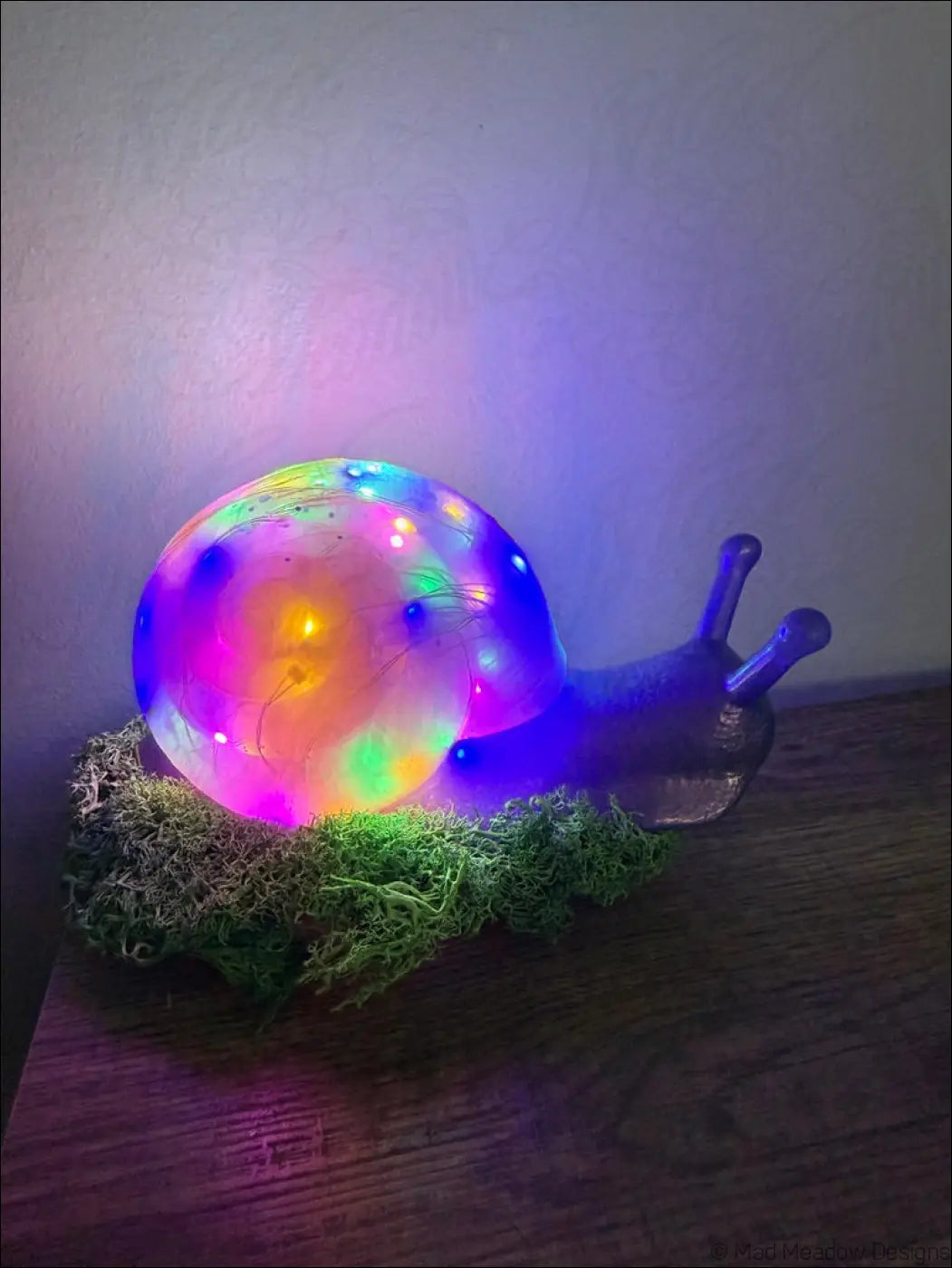 A glowing translucent led lamp shaped like a giant pastel blue and purple snail with green moss and color change USB light