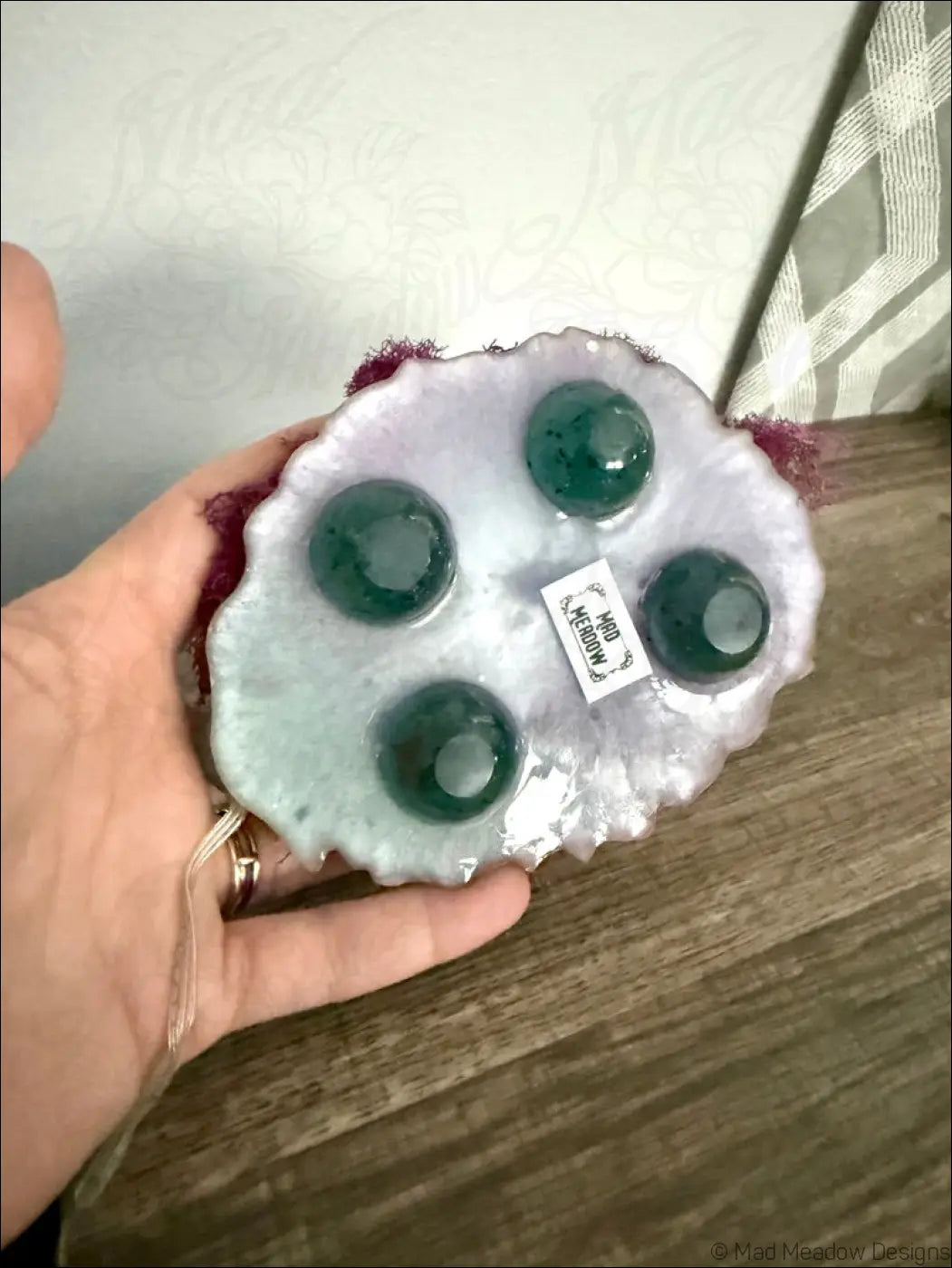 A hand holds a light purple resin coaster with green stones for the giant pastel blue and purple snail usb light