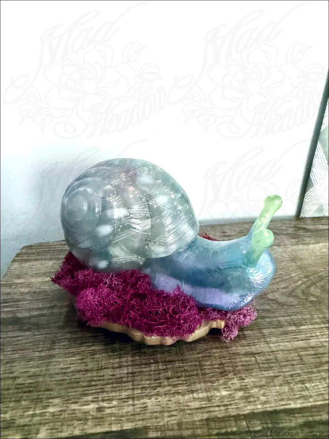 A translucent iridescent giant pastel blue and purple snail figurine with green antennae on vibrant pink moss light usb controlled