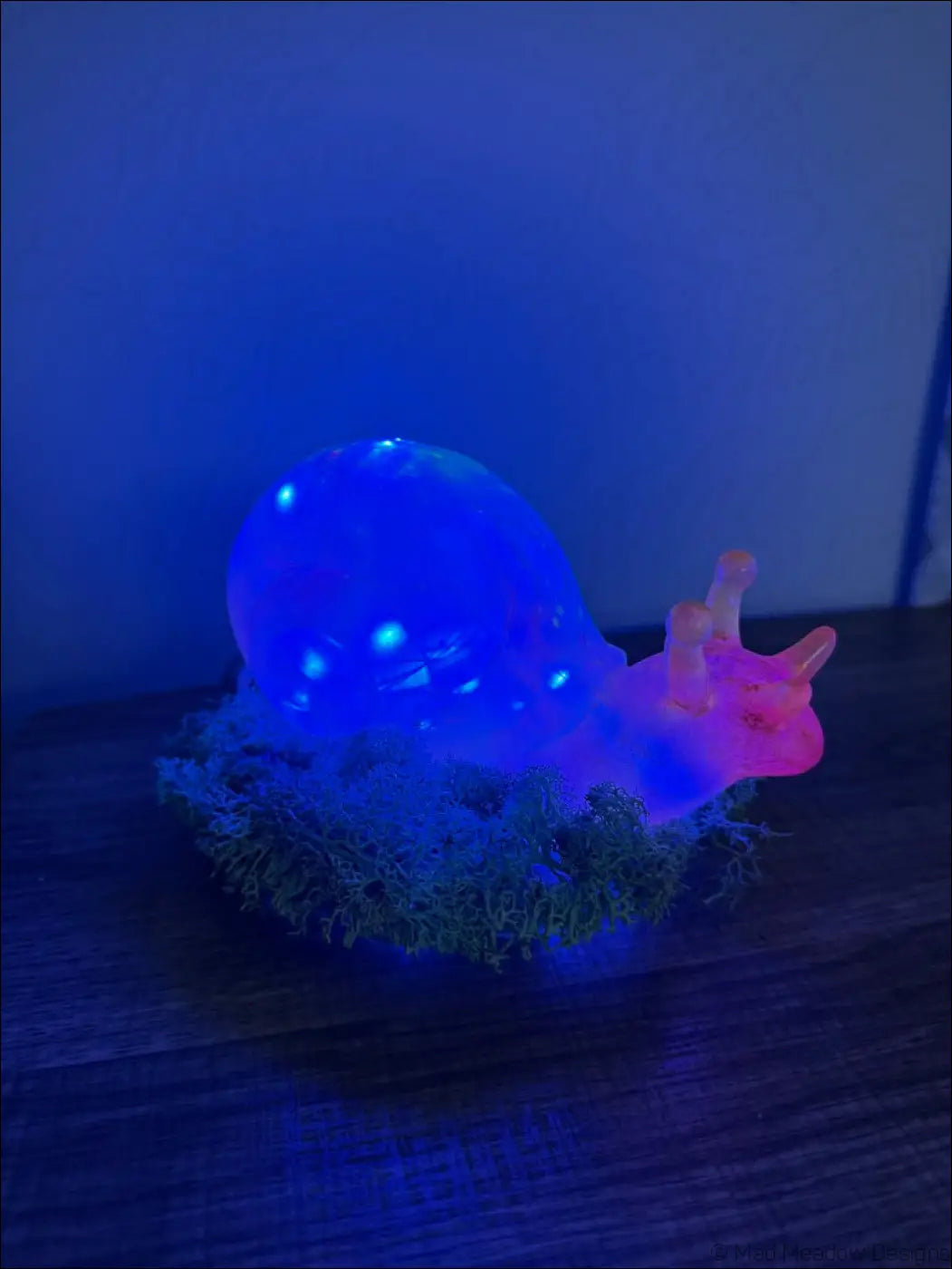 A glowing blue and pink giant snail figurine with translucent shell resting on artificial moss rgb usb or battery light