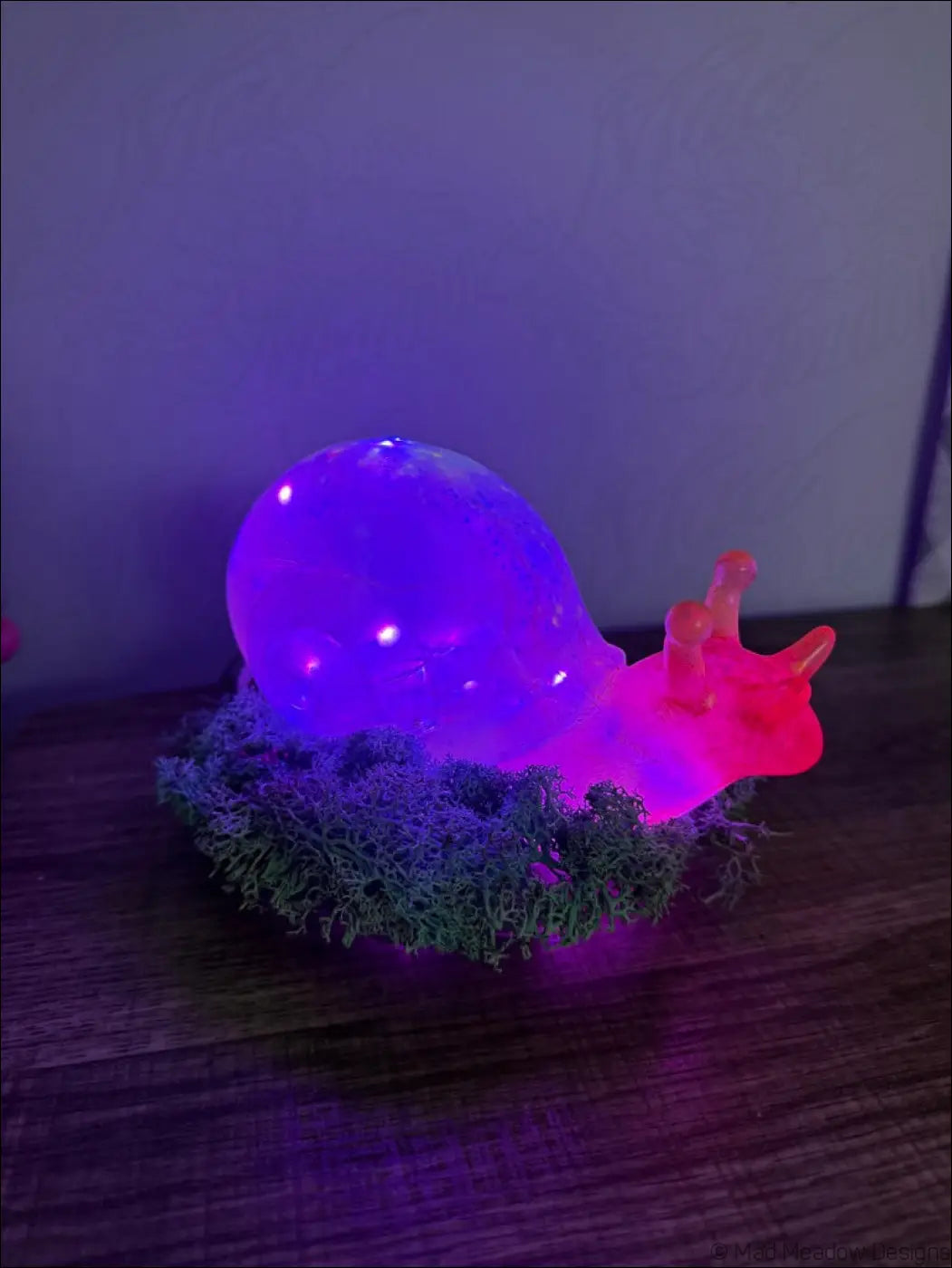 A glowing purple and pink led snail lamp with a translucent shell resting on moss from the giant pink gold rgb usb battery light
