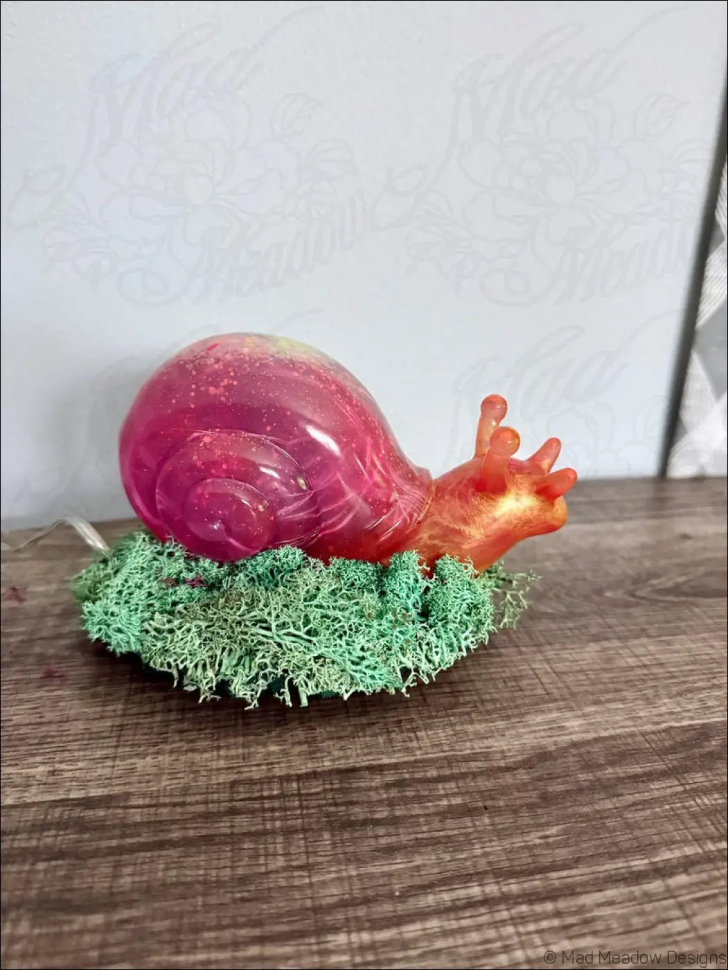A giant pink and gold translucent resin snail figurine with a glossy shell on green moss for rgb usb or battery light