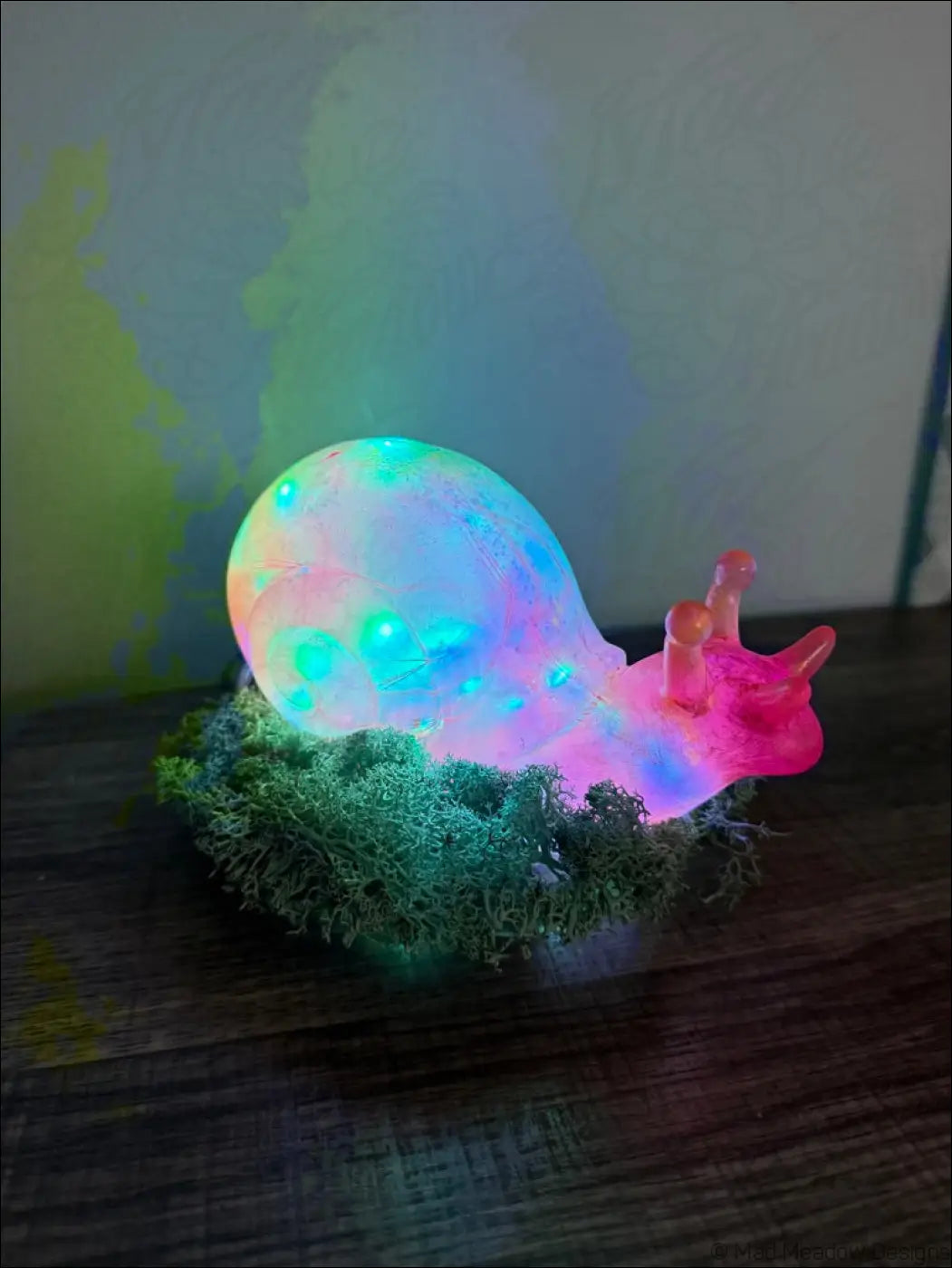 A giant pink and gold translucent snail led lamp with a rainbow shell resting on green moss for usb or battery use