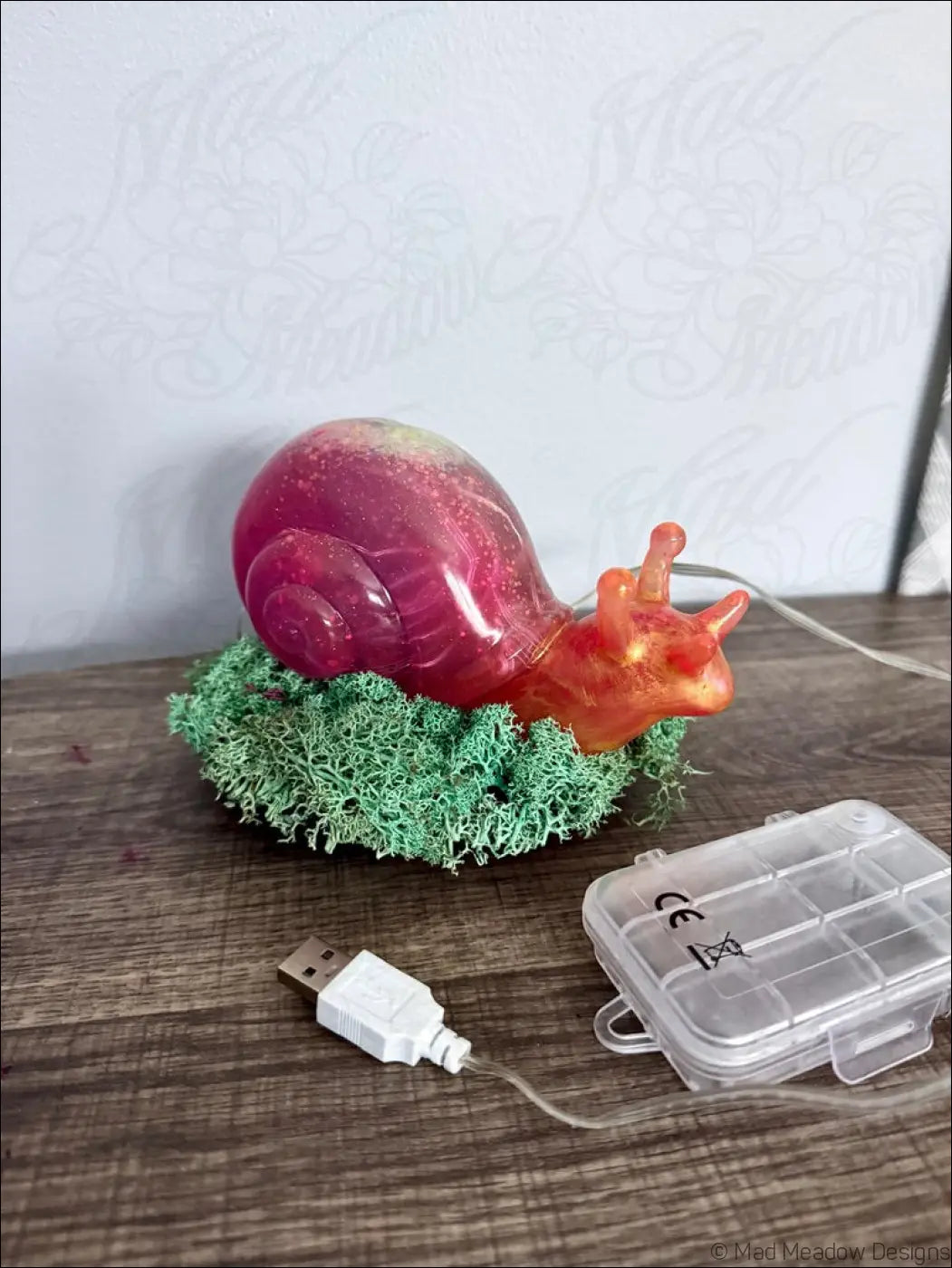 Giant pink and gold snail shaped led lamp with translucent resin finish resting on a green mossy base with rgb light