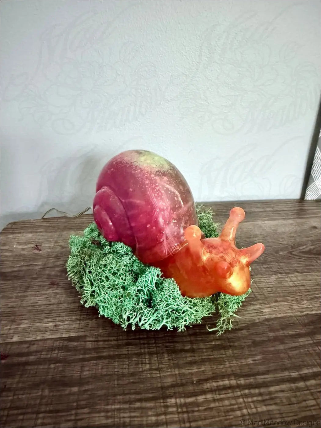 A translucent giant pink and gold snail figurine with a gradient shell on green moss with rgb usb or battery light