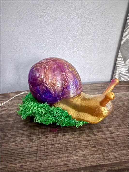 A giant purple and gold snail-shaped usb lamp with translucent iridescent shell resting on green moss material