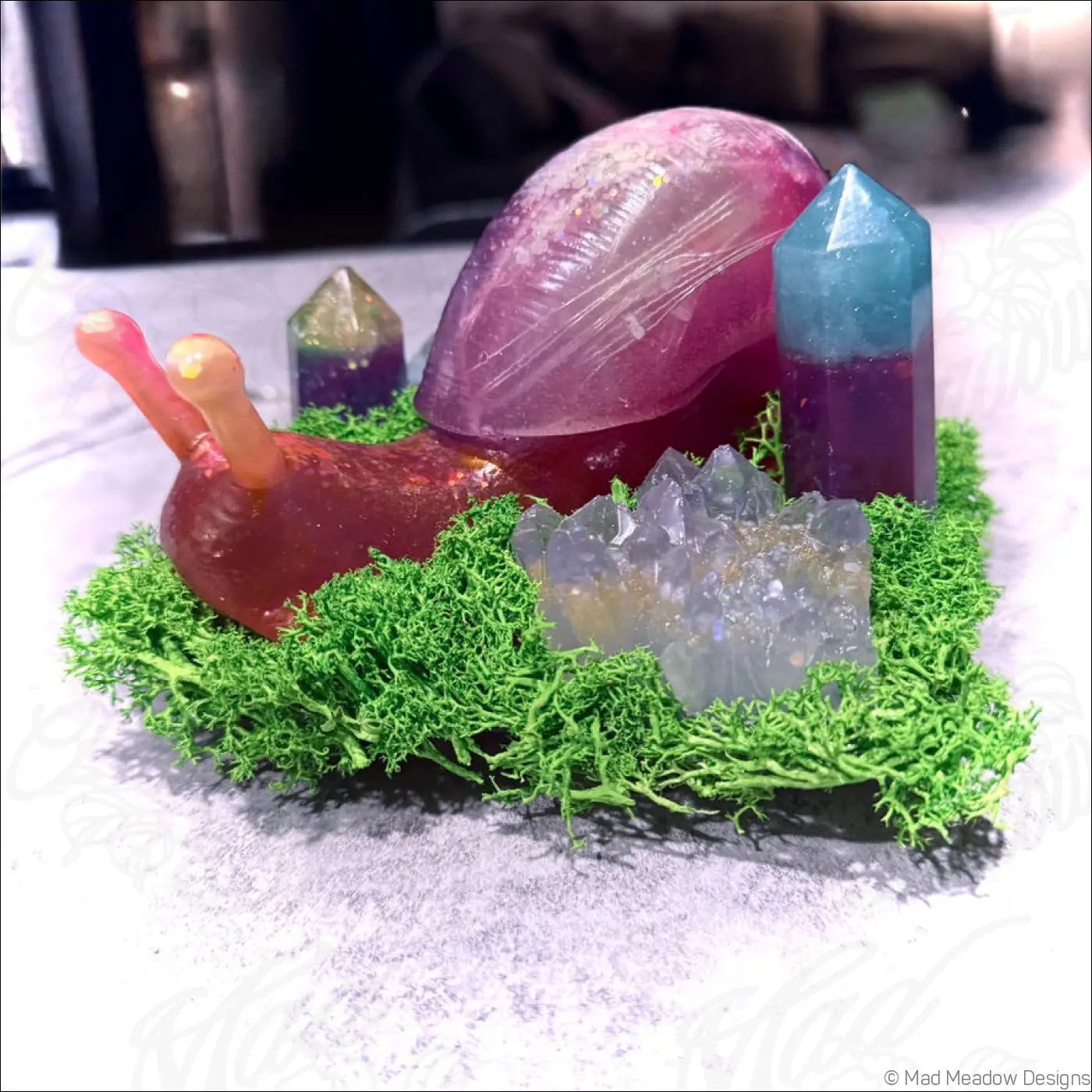 A translucent resin giant snail with a pinkish-purple shell and orange antennae on green moss with crystals rgb usb light