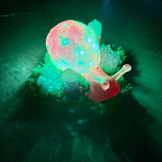 A giant snail led light glowing pink and teal with blue lights resting on green moss for usb or battery use