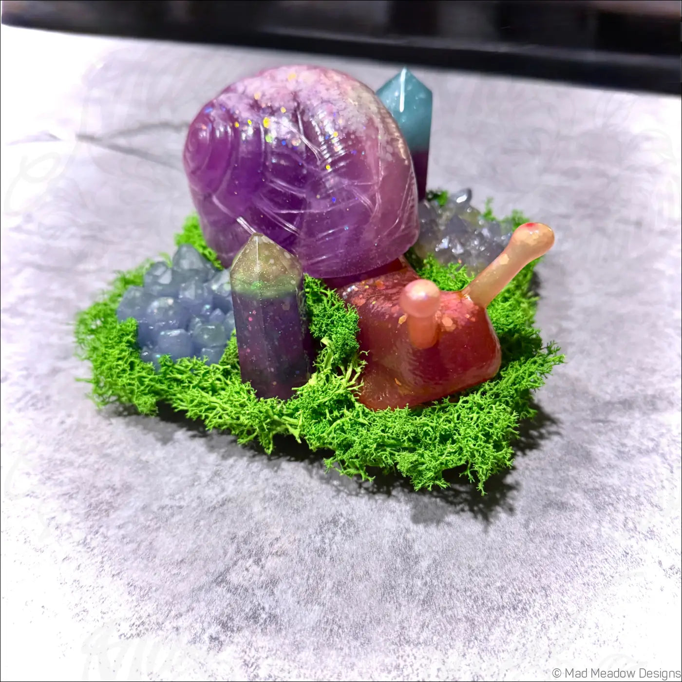 A translucent purple and red resin giant snail with a glittery shell nestled in green moss and colorful crystals rgb usb light