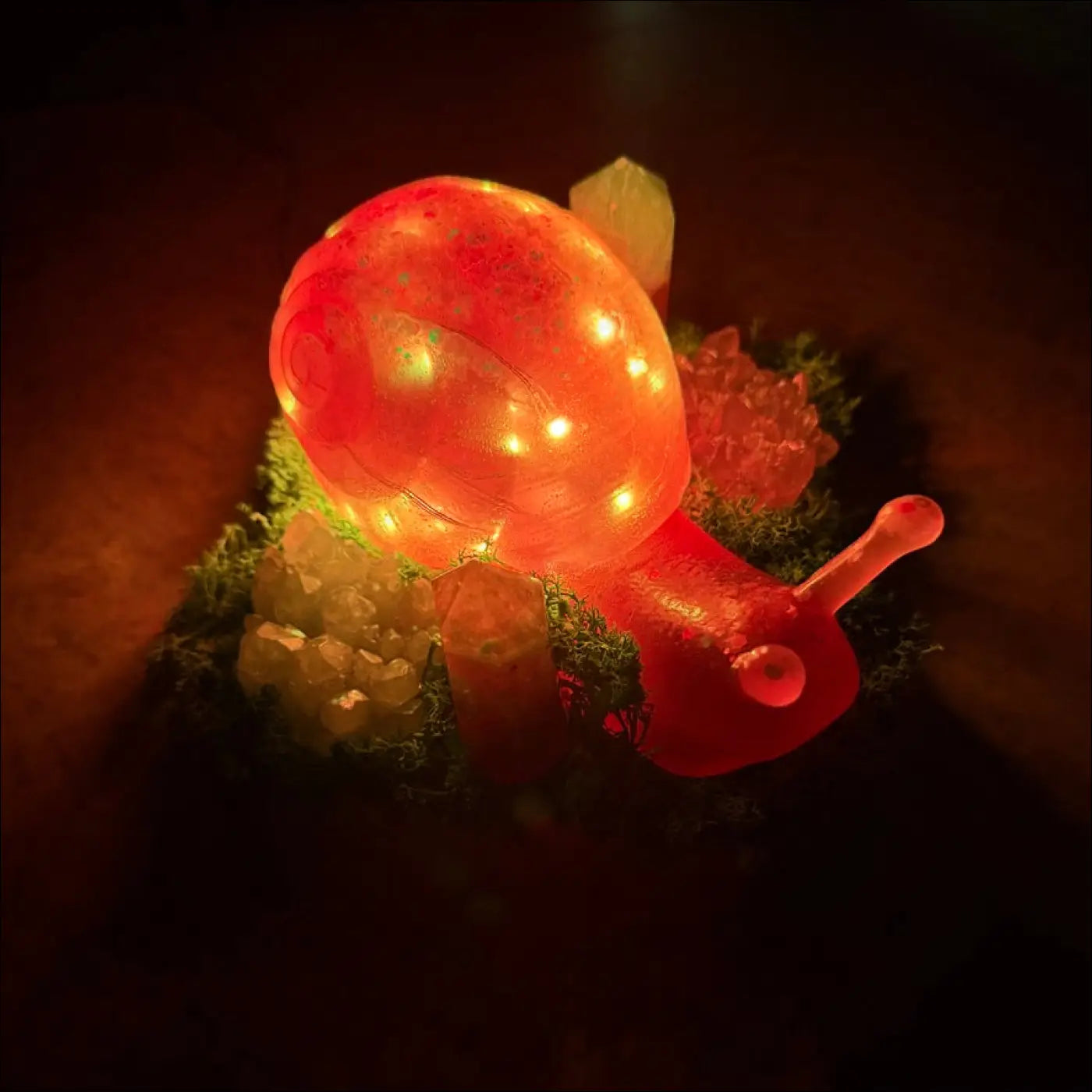 A glowing red giant snail figurine with translucent shell and embedded rgb lights resting on mossy terrain