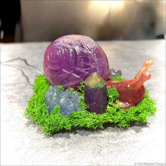 A translucent purple giant snail figurine with iridescent shell and reddish-brown body on green moss with crystals usb light