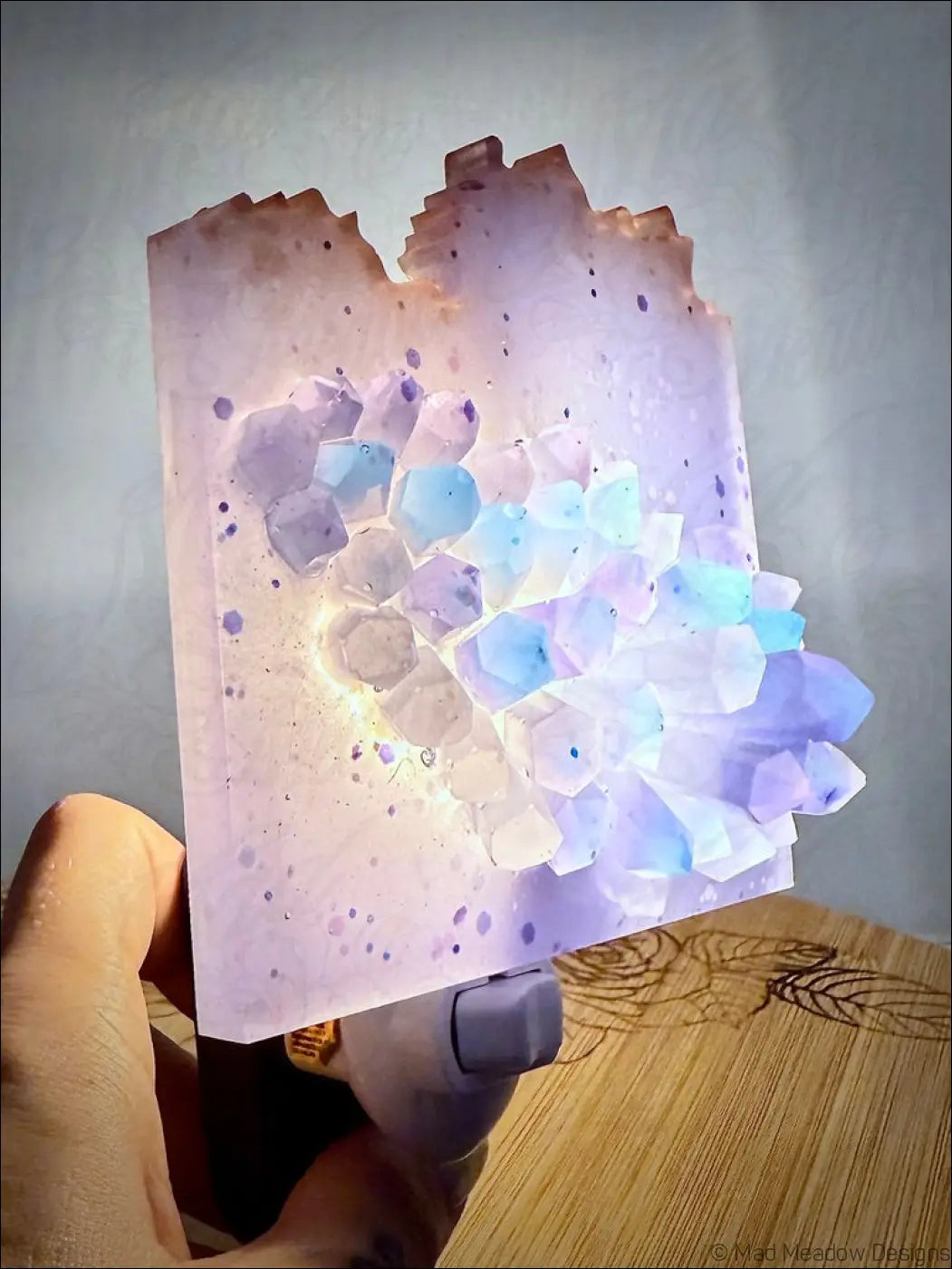 Glowing crystal cluster wall night light in purple and blue resin with a textured faceted design on a plug-in base